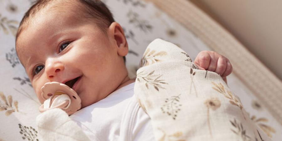 hydrofiele luiers header Vol Verwachting - Lachende baby met speen gewikkeld in hydrofiele doek